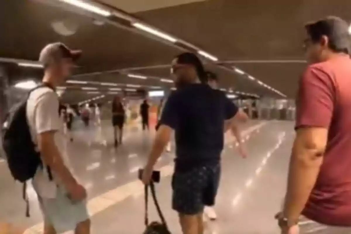 Tres homes caminen per una estació de metro il·luminada mentre altres persones es veuen al fons