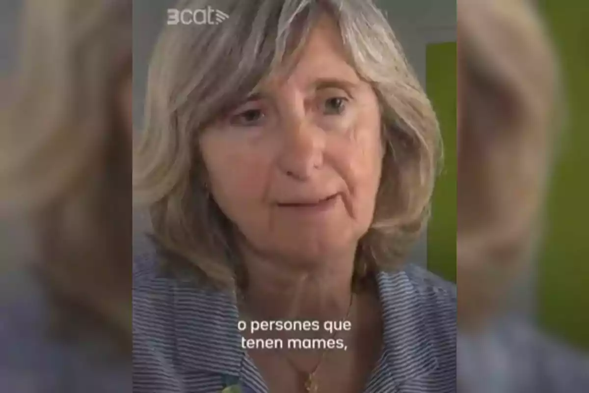 Mujer de cabello canoso y corto con expresión seria, lleva una blusa de rayas y un collar, en la parte superior izquierda aparece el logo de 3cat y en la parte inferior hay subtítulos en catalán.