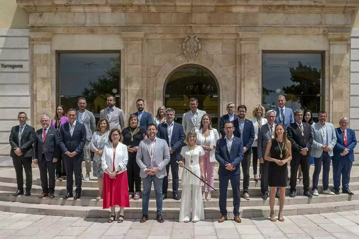 Un grupo de personas vestidas de manera formal posando para una foto frente a un edificio de piedra con grandes ventanas y una puerta arqueada Un grupo de personas vestidas de manera formal posando para una foto frente a un edificio de piedra con grandes ventanas y una puerta arqueada