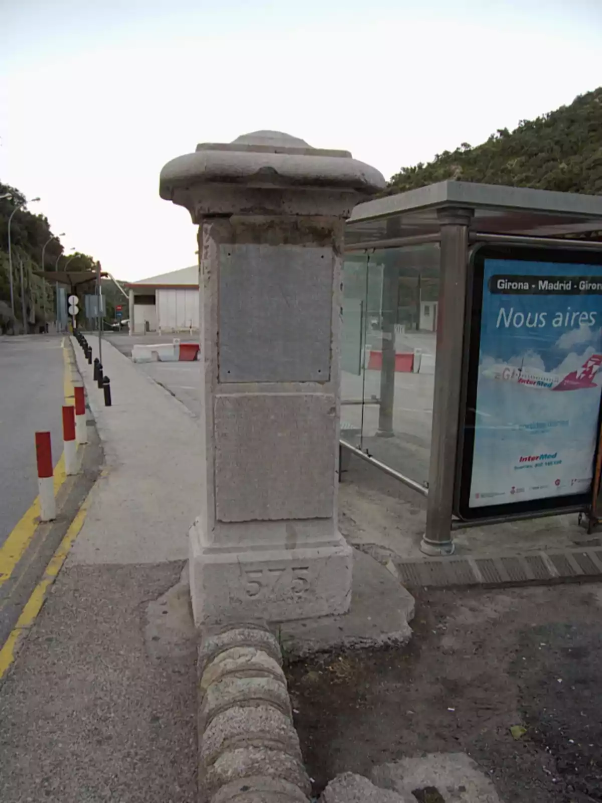 Antiga columna de pedra al costat d’una parada d’autobús en una vorera urbana Antiga columna de pedra al costat d’una parada d’autobús en una vorera urbana