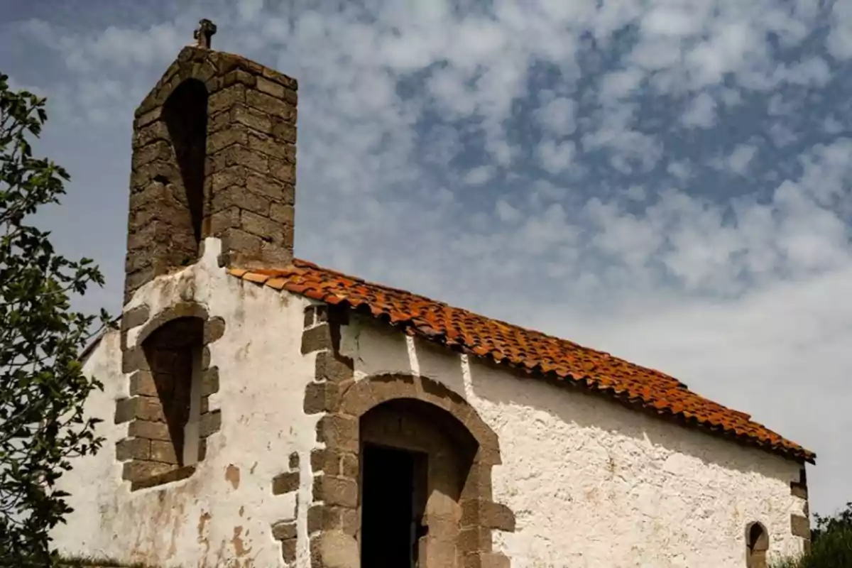 Pequeña iglesia de piedra con techo de tejas rojas bajo un cielo parcialmente nublado Pequeña iglesia de piedra con techo de tejas rojas bajo un cielo parcialmente nublado