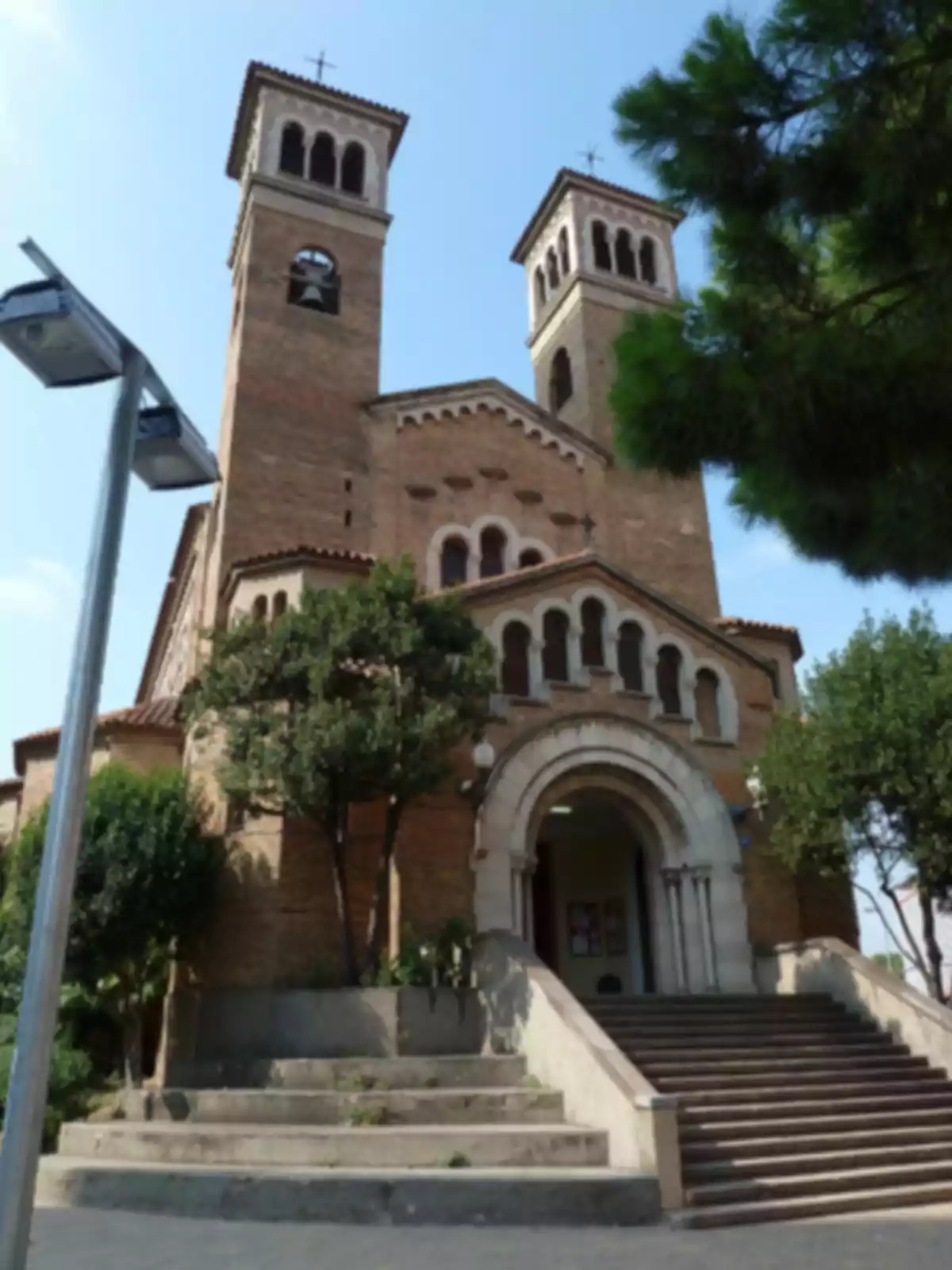 Façana d’una església de maó amb dues torres i una escalinata envoltada d’arbres Façana d’una església de maó amb dues torres i una escalinata envoltada d’arbres