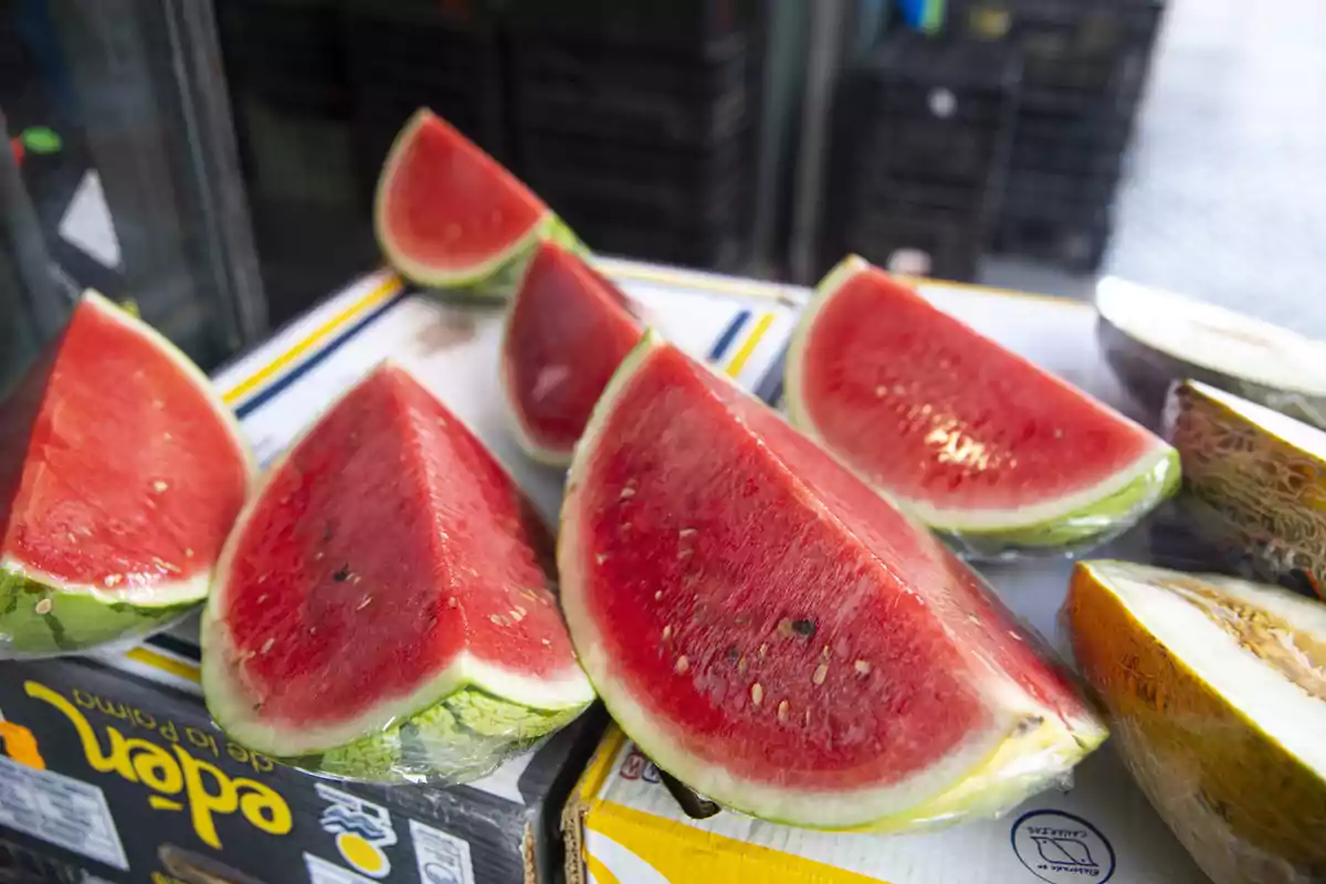 Llesques de síndria fresca embolicades amb plàstic sobre una caixa en un mercat Llesques de síndria fresca embolicades amb plàstic sobre una caixa en un mercat