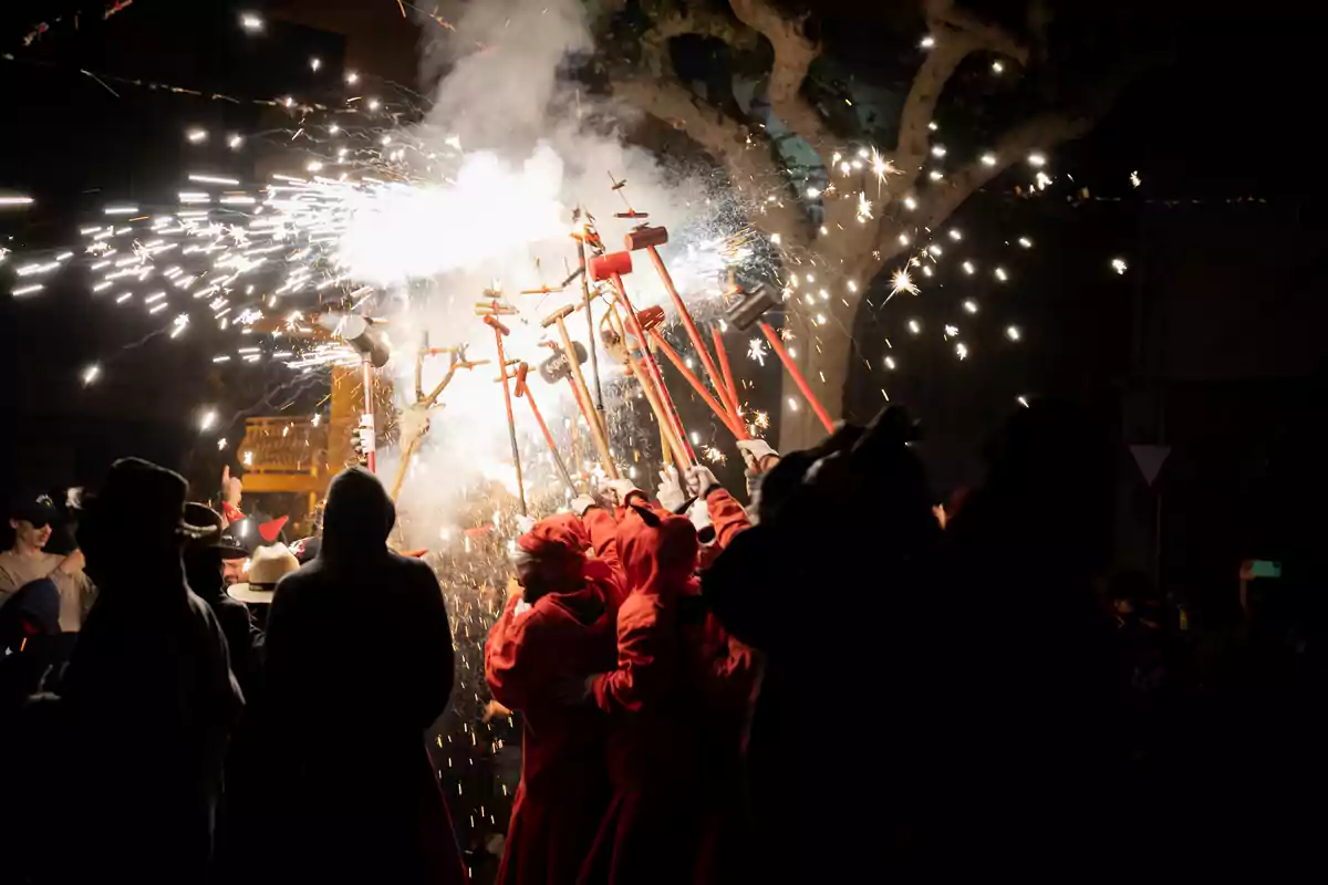 Personas vestidas con túnicas rojas celebran una fiesta tradicional con fuegos artificiales y chispas en la noche Personas vestidas con túnicas rojas celebran una fiesta tradicional con fuegos artificiales y chispas en la noche