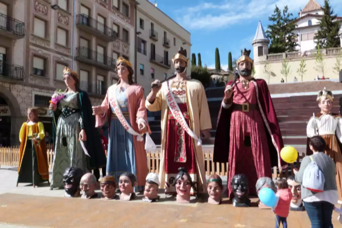 Desfile de figuras gigantes y cabezudos en una plaza con personas observando y edificios al fondo Desfile de figuras gigantes y cabezudos en una plaza con personas observando y edificios al fondo