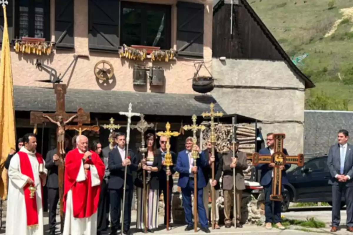 Un grupo de personas vestidas de manera formal y religiosa sostiene varias cruces frente a una casa de estilo rústico en un entorno rural, durante lo que parece ser una ceremonia religiosa al aire libre. Un grupo de personas vestidas de manera formal y religiosa sostiene varias cruces frente a una casa de estilo rústico en un entorno rural, durante lo que parece ser una ceremonia religiosa al aire libre.