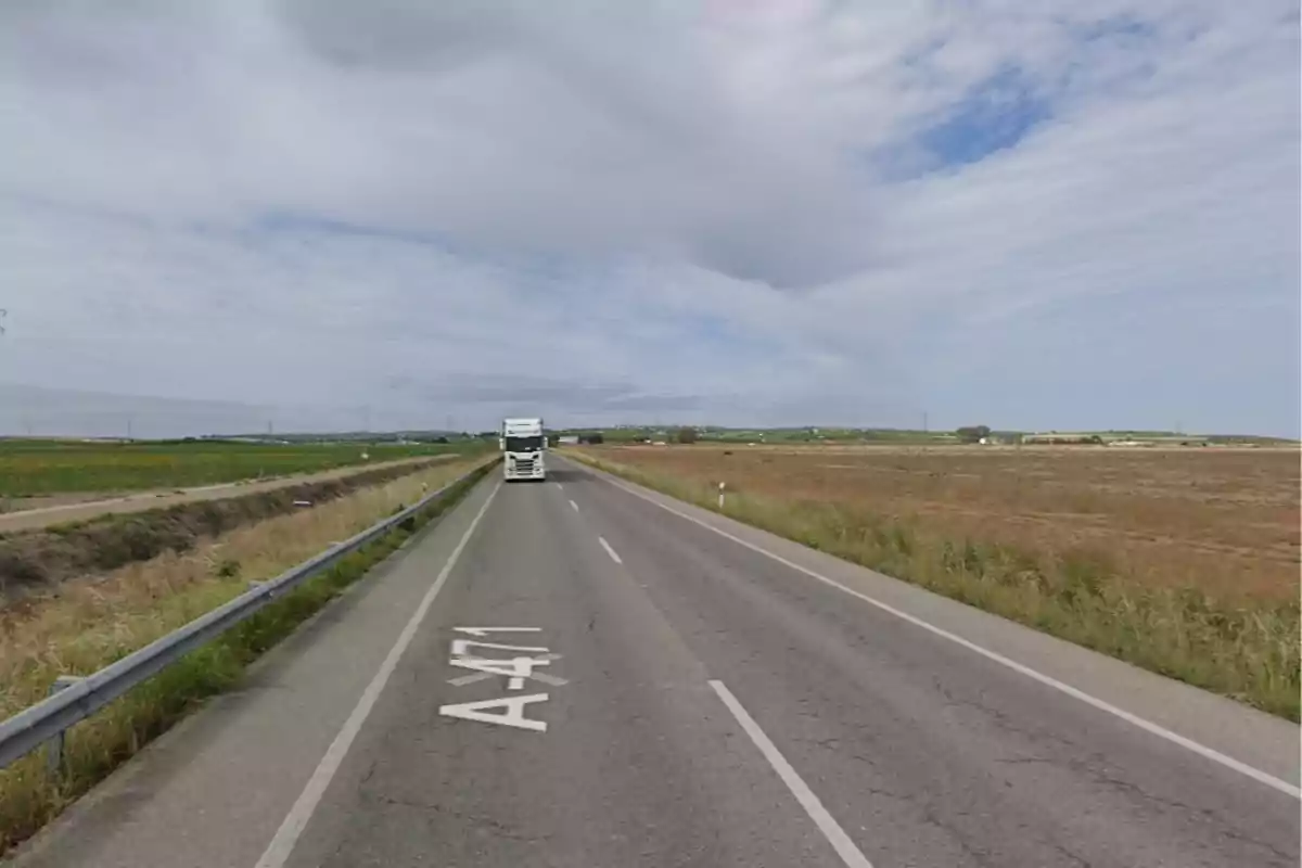 Carretera rural de dos carrils amb un camió blanc circulant i camps a banda i banda sota un cel parcialment ennuvolat Carretera rural de dos carrils amb un camió blanc circulant i camps a banda i banda sota un cel parcialment ennuvolat