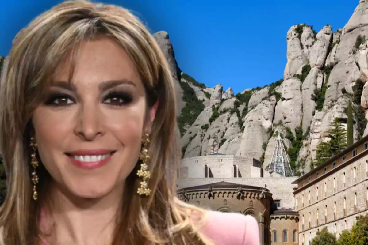 Dona somrient amb cabells rossos i arracades daurades davant d’un paisatge de muntanyes rocoses i un edifici històric sota un cel blau