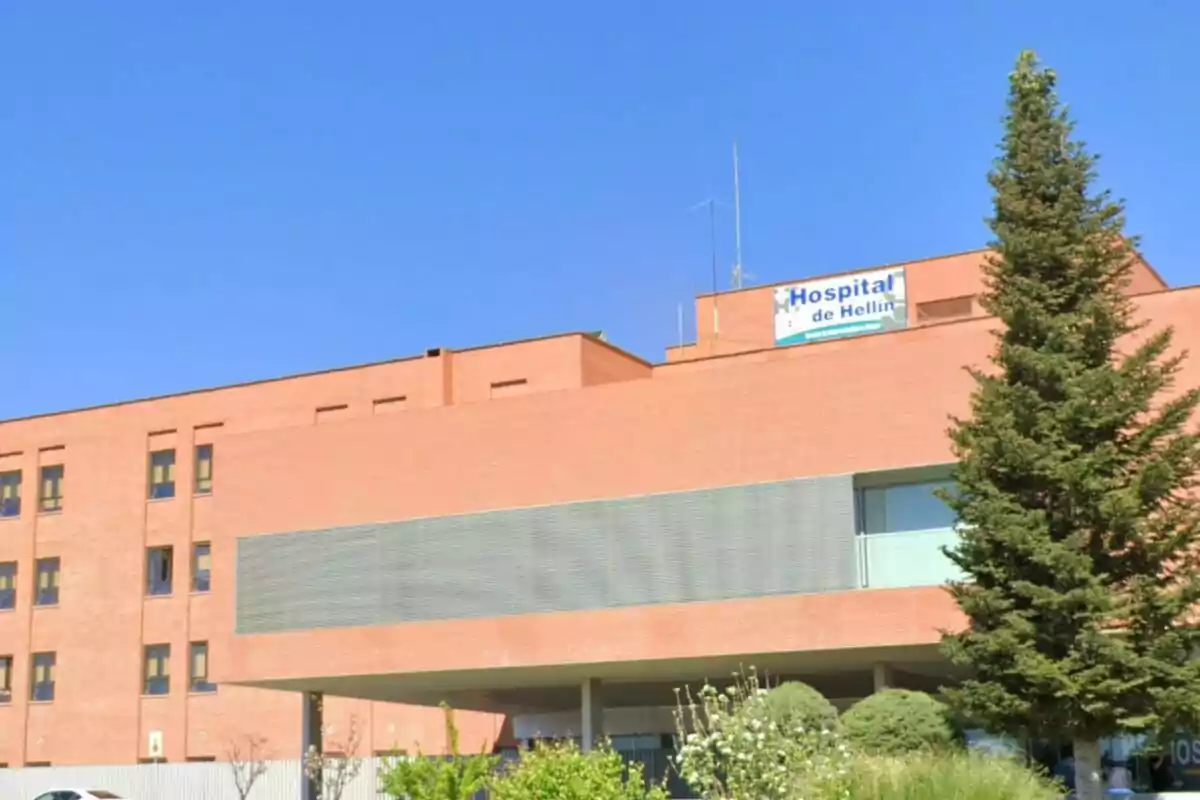 Fachada de un hospital de ladrillo con un letrero que dice Hospital de Hellín y un árbol grande al frente. Fachada de un hospital de ladrillo con un letrero que dice Hospital de Hellín y un árbol grande al frente.