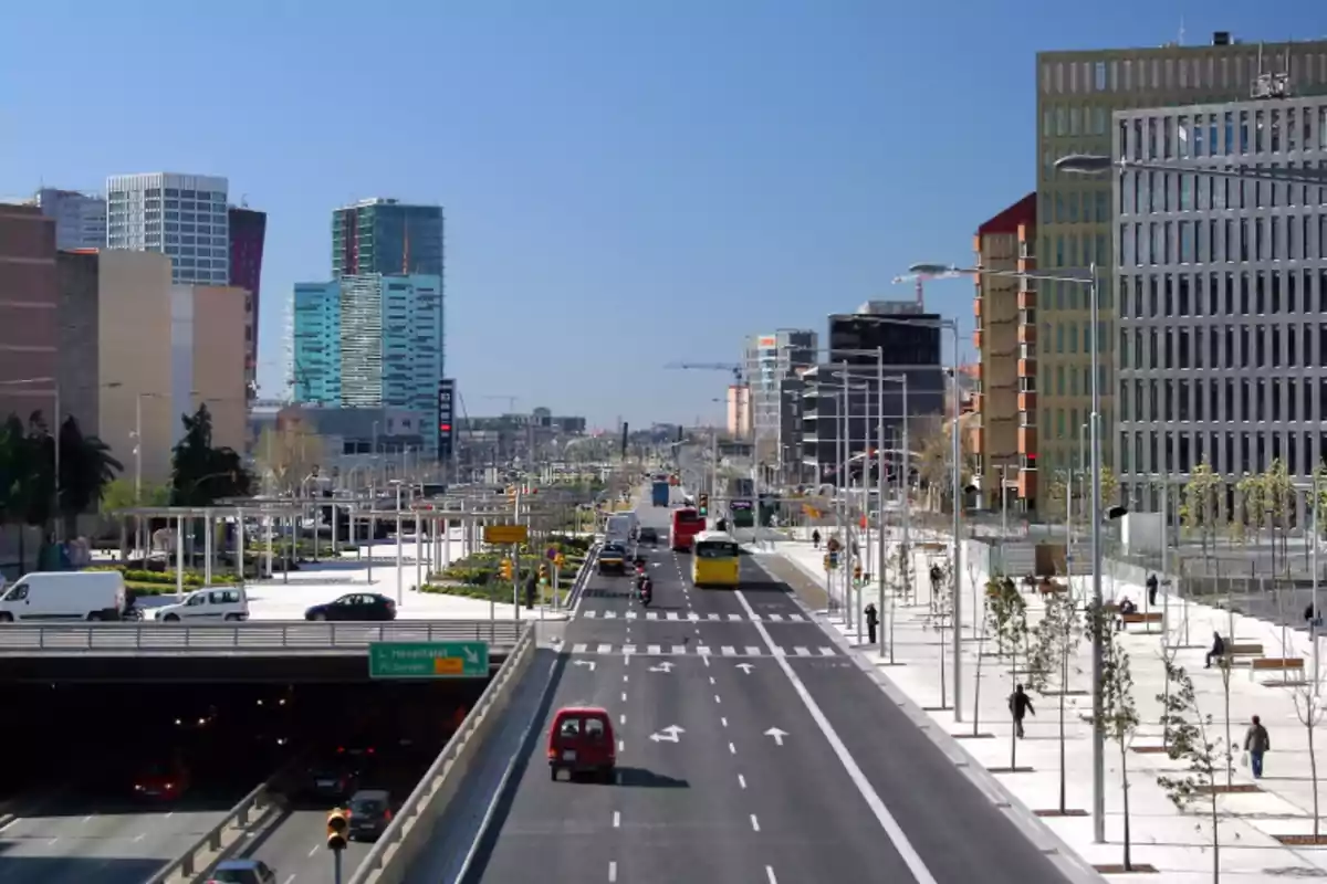 Avinguda ampla amb diversos carrils, edificis moderns als costats, arbres joves i persones caminant per les voreres en un dia assolellat. Avinguda ampla amb diversos carrils, edificis moderns als costats, arbres joves i persones caminant per les voreres en un dia assolellat.