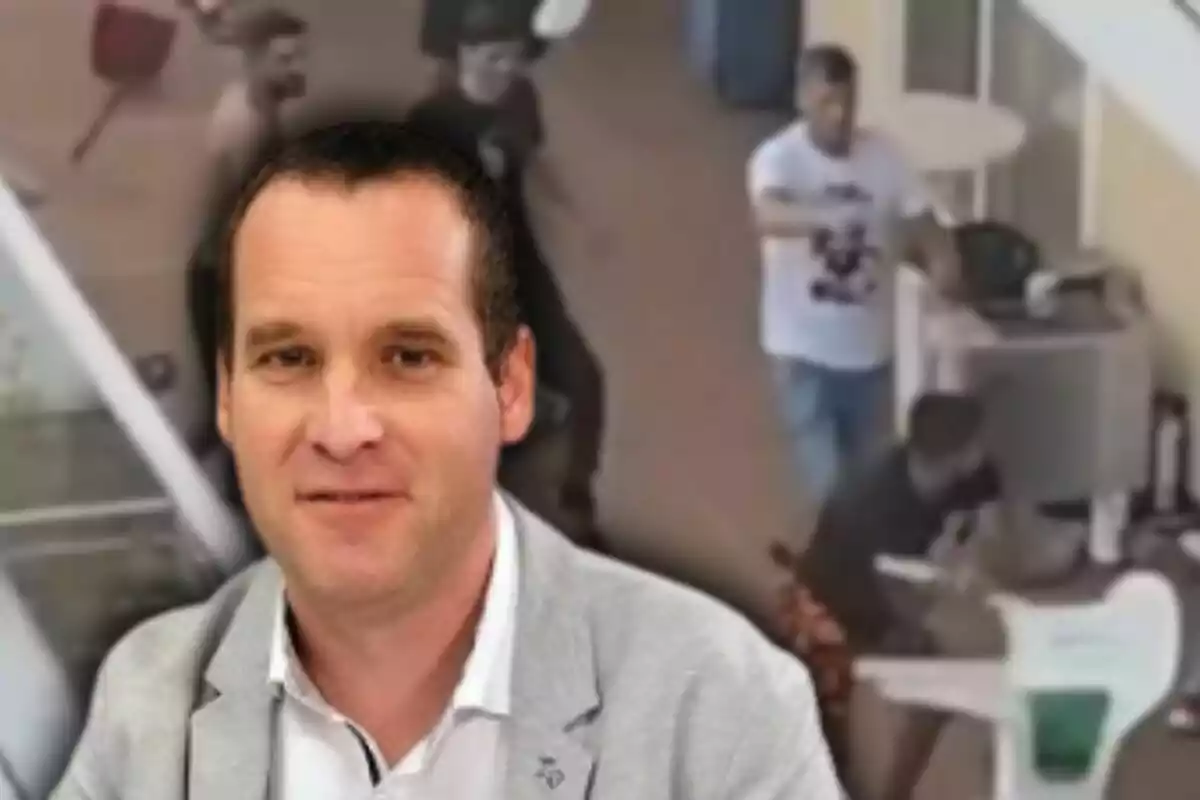 Home de cabell curt i jaqueta grisa en primer pla amb una escena borrosa de diverses persones al fons en un ambient interior