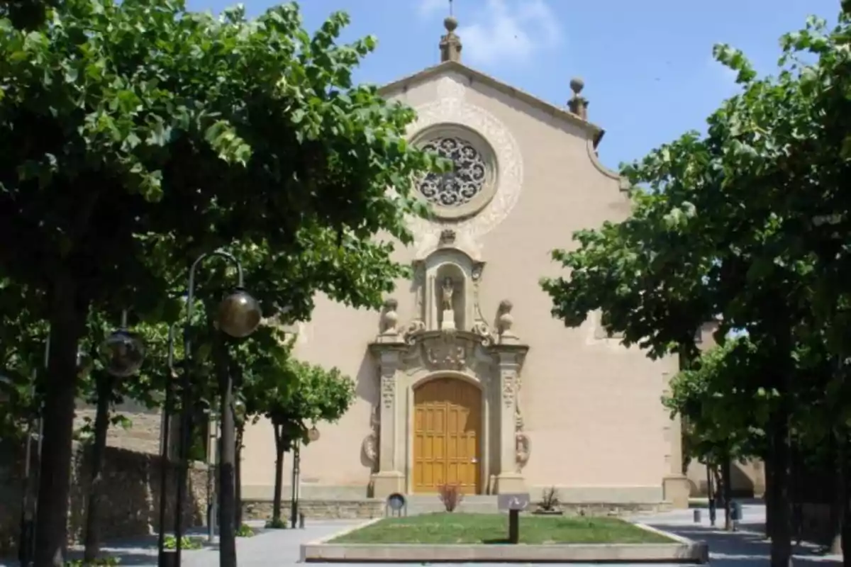 Fachada de una iglesia antigua rodeada de árboles y farolas en un día soleado Fachada de una iglesia antigua rodeada de árboles y farolas en un día soleado