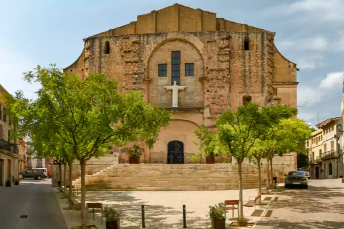 Fachada de una iglesia antigua de ladrillo con una escultura de Cristo y una plaza con árboles y bancos al frente Fachada de una iglesia antigua de ladrillo con una escultura de Cristo y una plaza con árboles y bancos al frente