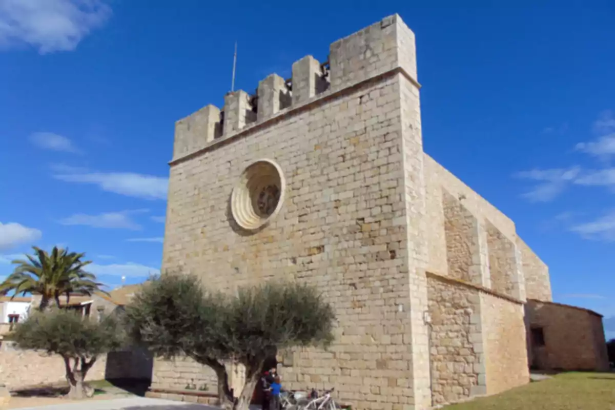 Església de pedra amb façana fortificada i rosassa circular sota un cel blau Església de pedra amb façana fortificada i rosassa circular sota un cel blau