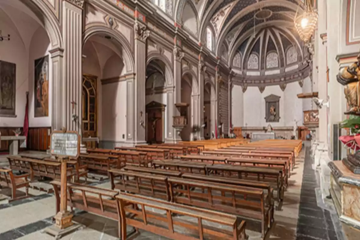 Interior d’una església amb bancs de fusta, columnes altes i un altar al fons sota una cúpula decorada Interior d’una església amb bancs de fusta, columnes altes i un altar al fons sota una cúpula decorada