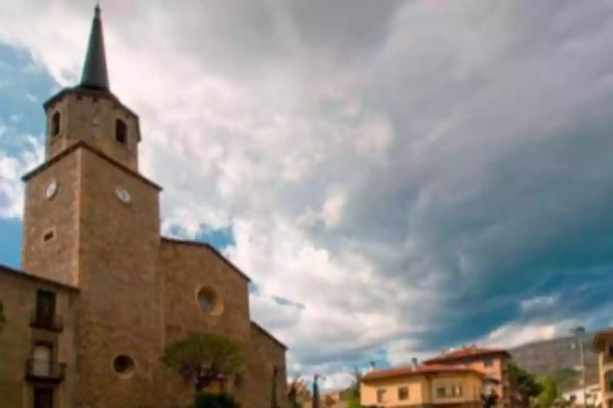 Iglesia de piedra con torre y reloj bajo un cielo nublado en un pueblo Iglesia de piedra con torre y reloj bajo un cielo nublado en un pueblo