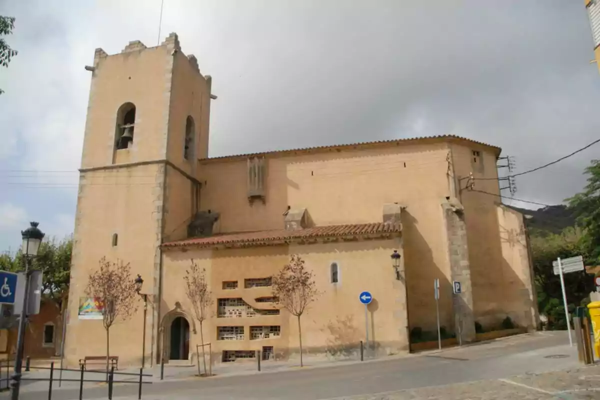 Iglesia antigua de paredes color beige con una torre campanario y árboles pequeños en la acera frente al edificio Iglesia antigua de paredes color beige con una torre campanario y árboles pequeños en la acera frente al edificio