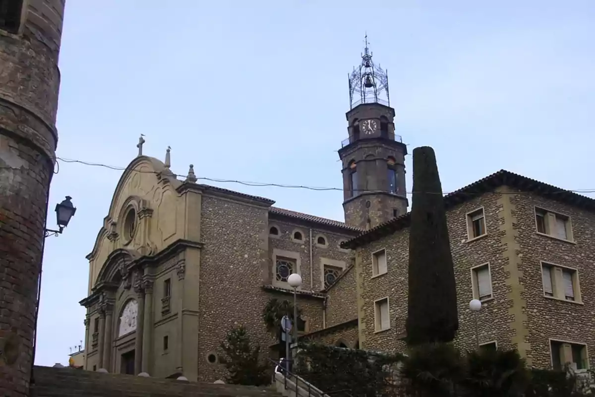 Fachada de una iglesia antigua con una torre de reloj y edificios de piedra a su alrededor en un día despejado Fachada de una iglesia antigua con una torre de reloj y edificios de piedra a su alrededor en un día despejado