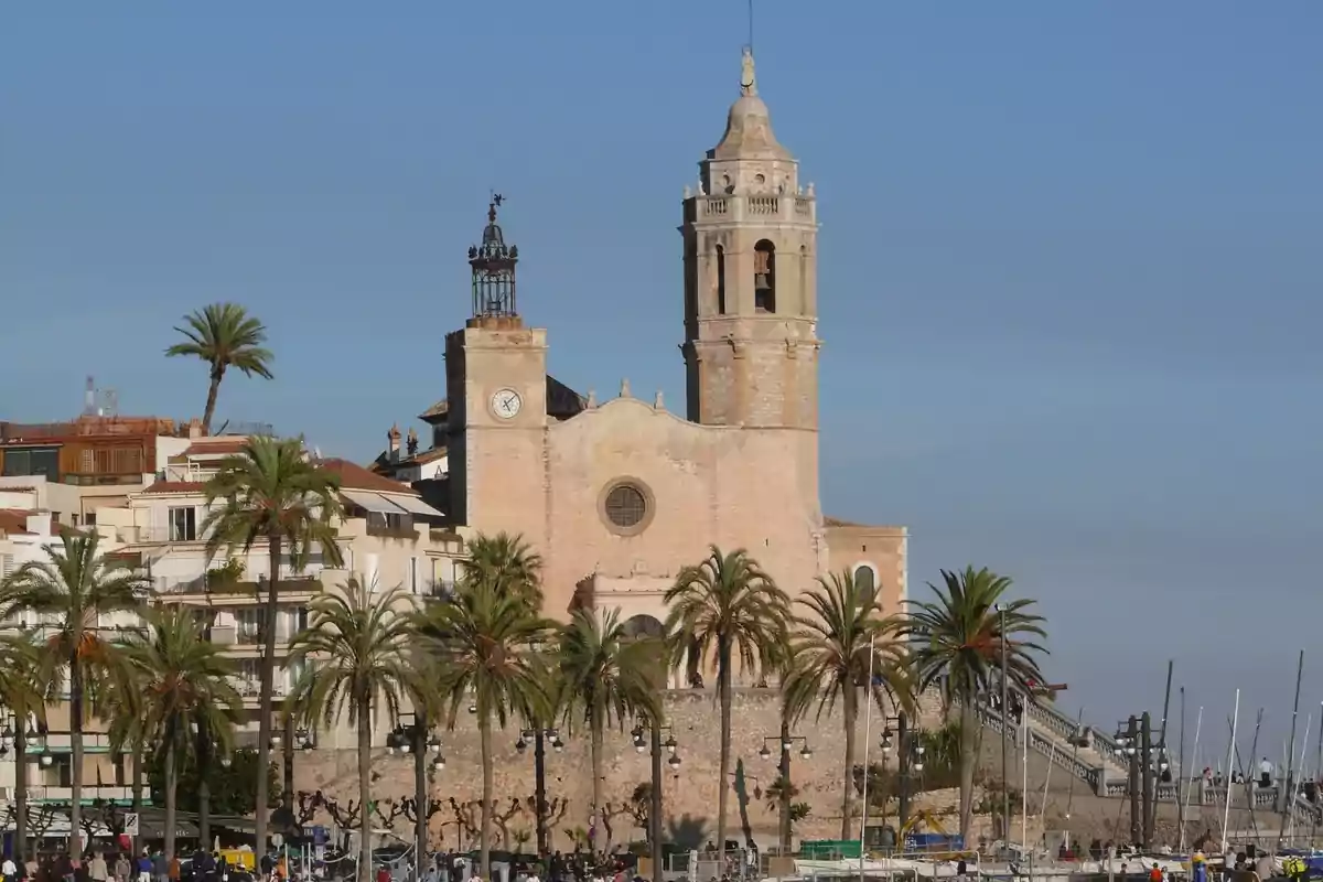 Iglesia antigua de piedra con una torre campanario rodeada de palmeras y edificios junto al mar en un día soleado Iglesia antigua de piedra con una torre campanario rodeada de palmeras y edificios junto al mar en un día soleado
