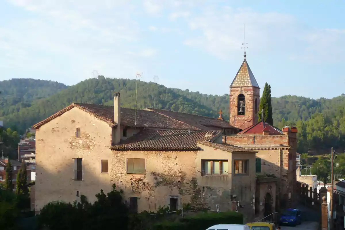 Edificio antiguo de piedra con tejado de tejas y campanario en un entorno rural rodeado de colinas y vegetación Edificio antiguo de piedra con tejado de tejas y campanario en un entorno rural rodeado de colinas y vegetación