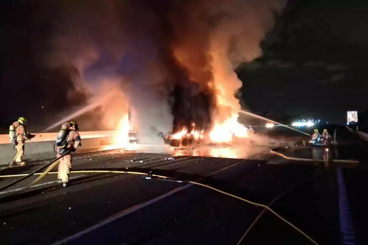Bombers combaten un incendi de gran magnitud en un vehicle sobre una carretera durant la nit Bombers combaten un incendi de gran magnitud en un vehicle sobre una carretera durant la nit