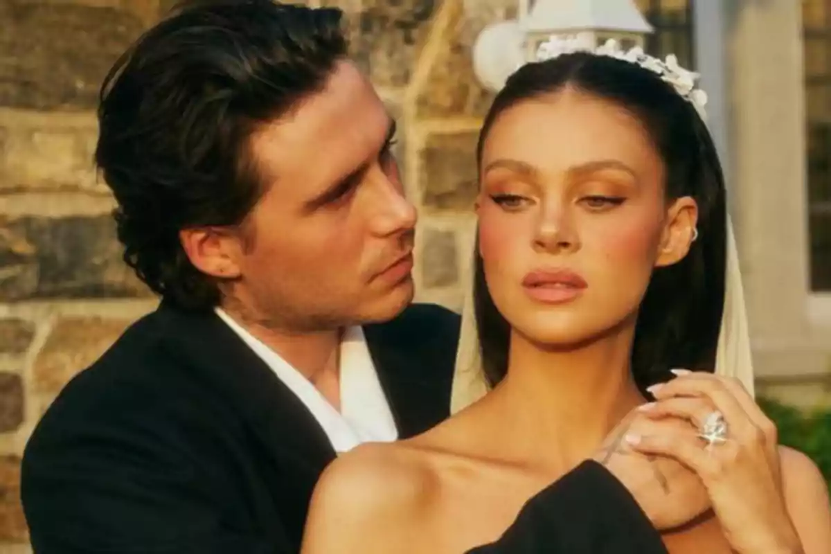 A couple dressed elegantly at a wedding, the man embraces the woman who is wearing a veil and a white tiara, both posing in front of a stone wall. A couple dressed elegantly at a wedding, the man embraces the woman who is wearing a veil and a white tiara, both posing in front of a stone wall.