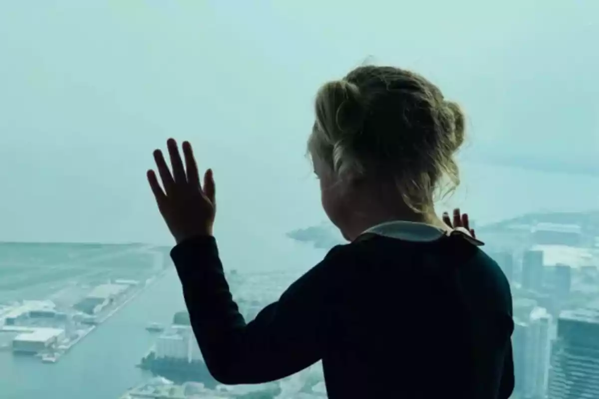 Girl with her back turned, hands resting on a large window, looking out over a city from above Girl with her back turned, hands resting on a large window, looking out over a city from above