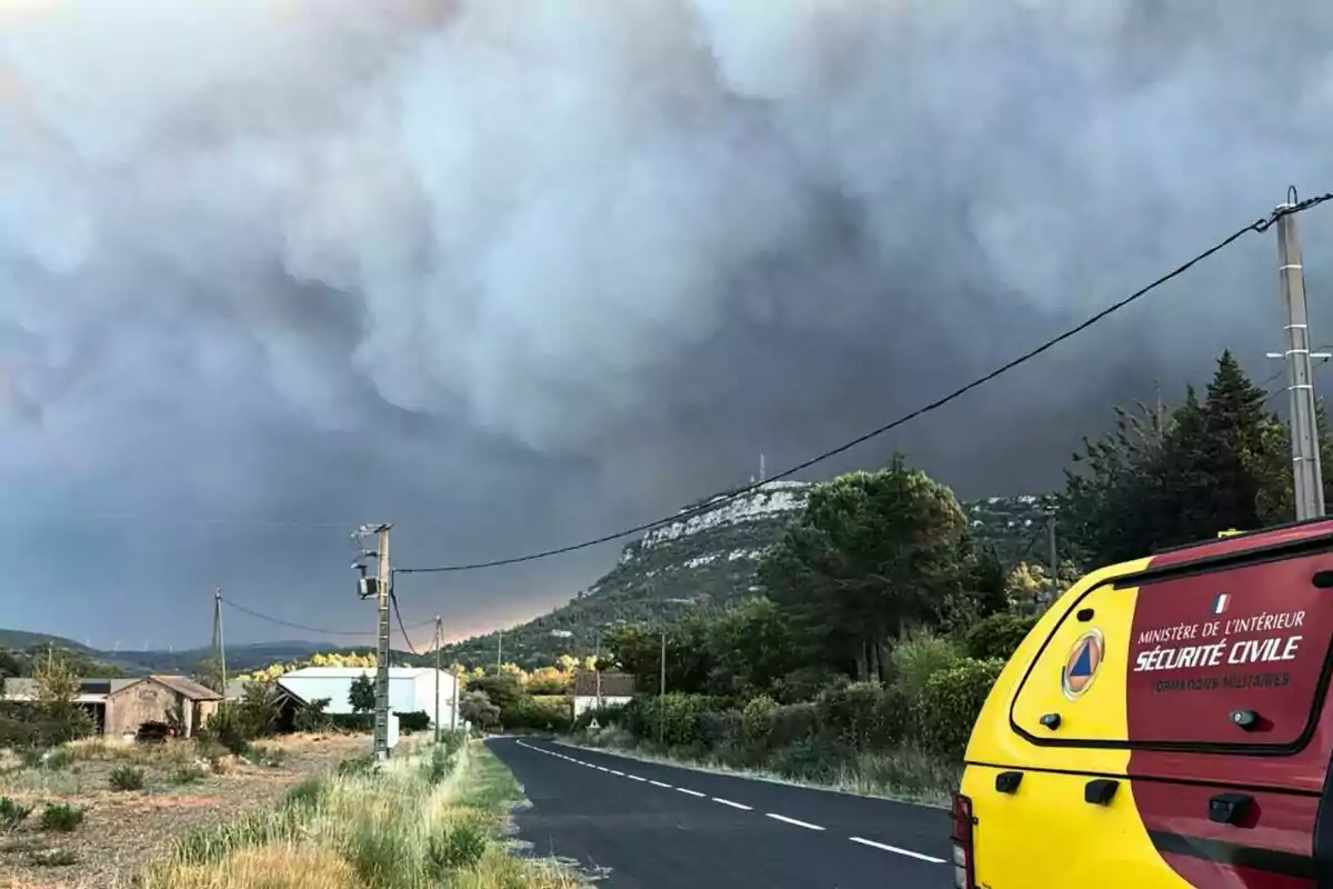 Nube densa de humo cubre el cielo cerca de una carretera rural con un vehículo de protección civil estacionado a un lado Nube densa de humo cubre el cielo cerca de una carretera rural con un vehículo de protección civil estacionado a un lado