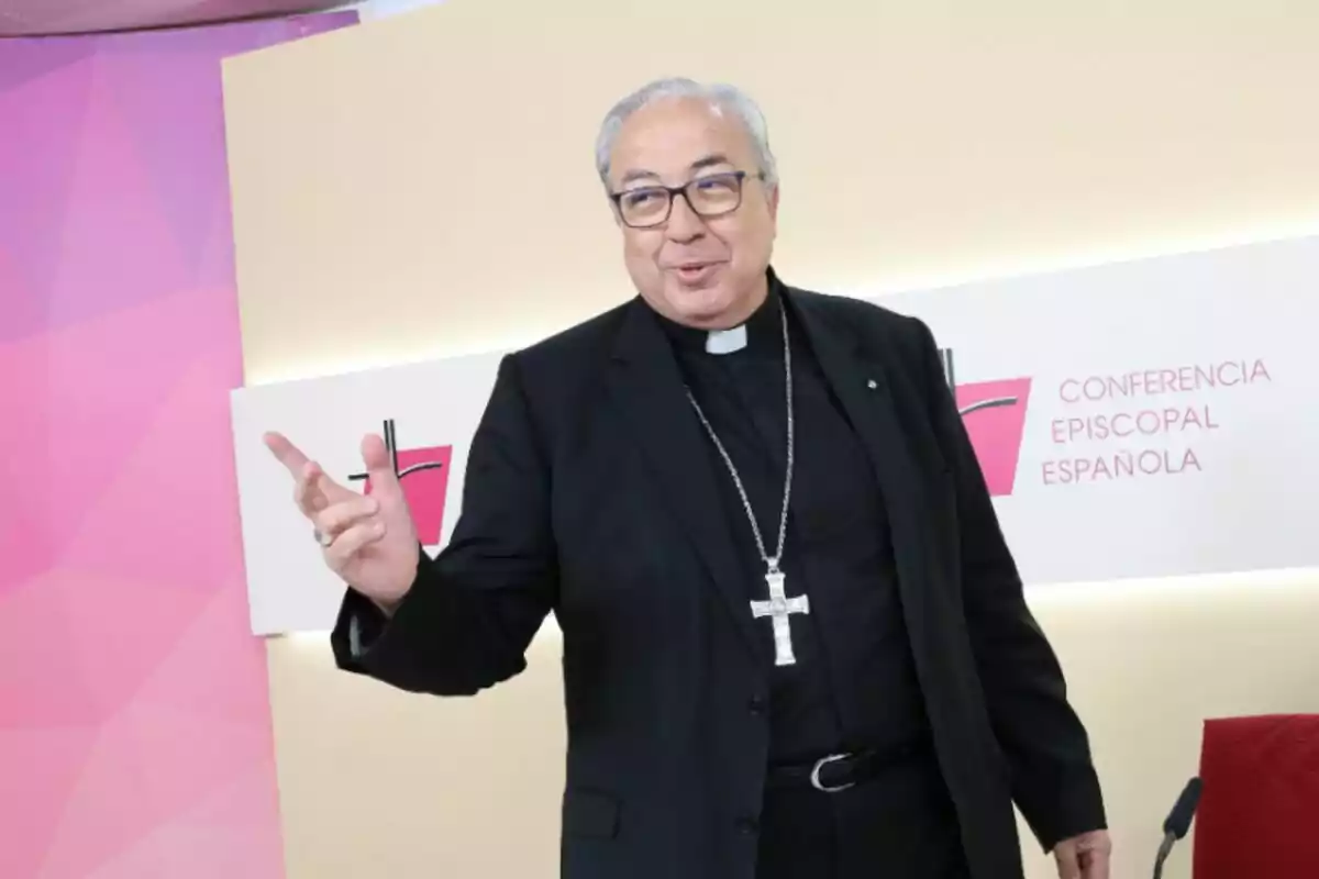 Francisco César García Magán, obispo, con gafas y vestimenta clerical negra sonríe y gesticula con la mano frente a un cartel de la Conferencia Episcopal Española Francisco César García Magán, obispo, con gafas y vestimenta clerical negra sonríe y gesticula con la mano frente a un cartel de la Conferencia Episcopal Española