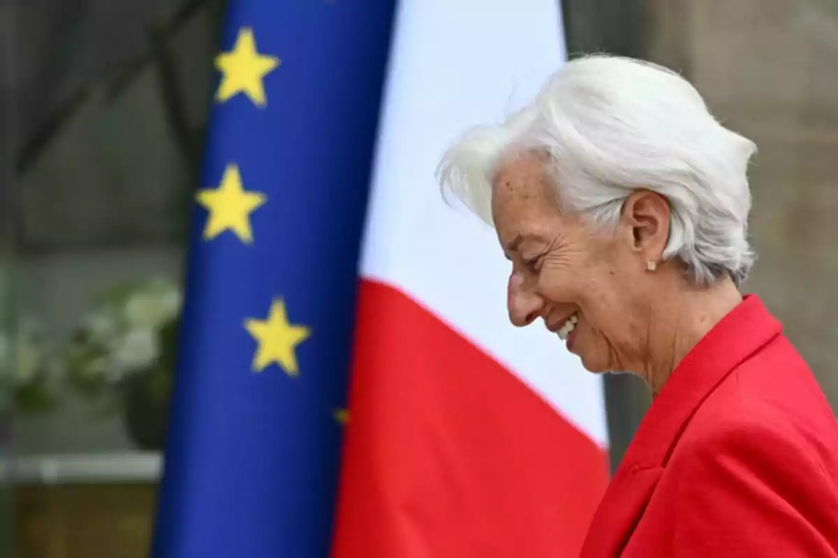 Christine Lagarde con cabello canoso y saco rojo sonríe frente a las banderas de la Unión Europea y Francia Christine Lagarde con cabello canoso y saco rojo sonríe frente a las banderas de la Unión Europea y Francia