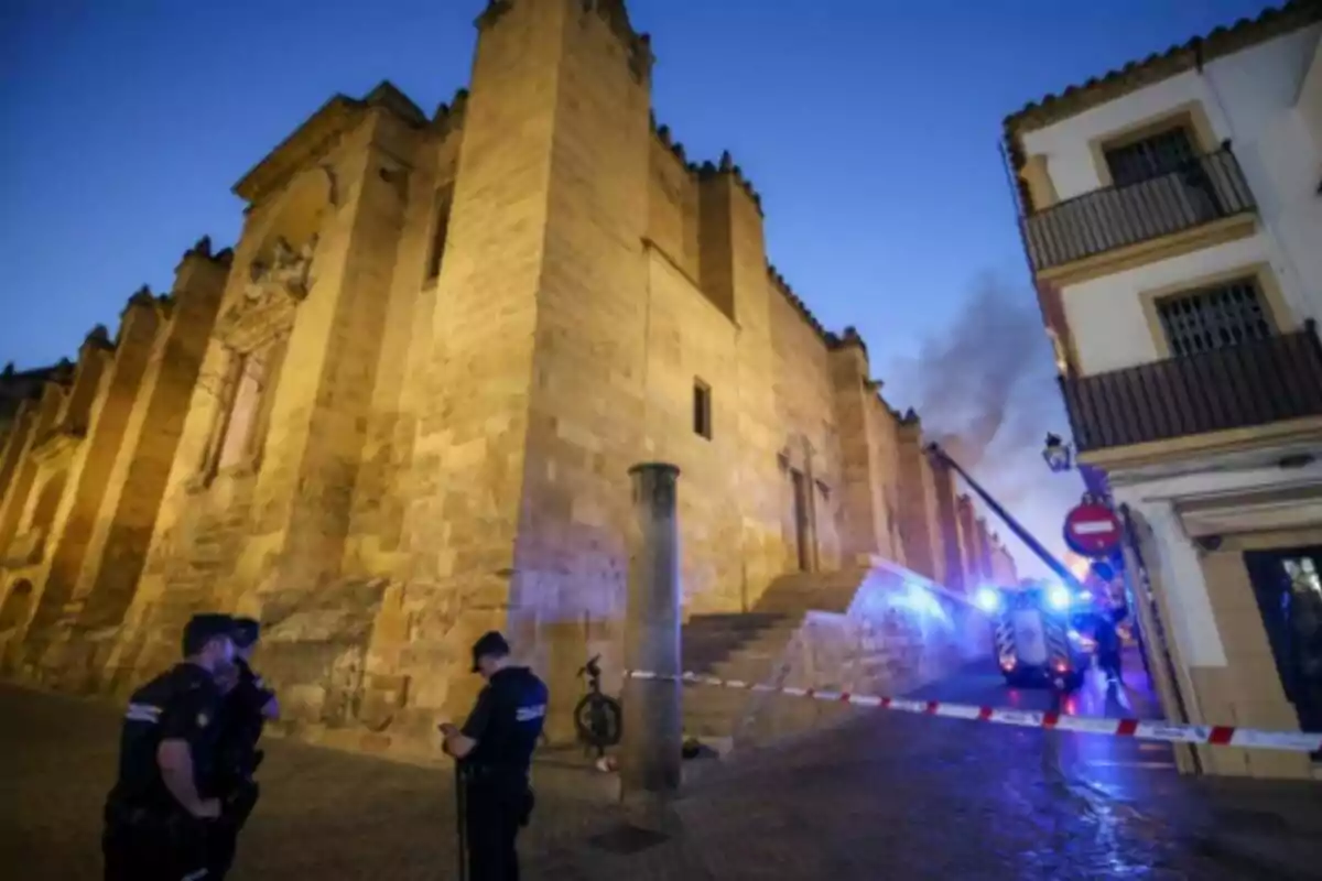 Policies i vehicles d’emergència atenen un incendi en un edifici històric, que és la Mesquita de Còrdova, al capvespre, amb fum visible i la zona acordonada. Policies i vehicles d’emergència atenen un incendi en un edifici històric, que és la Mesquita de Còrdova, al capvespre, amb fum visible i la zona acordonada.