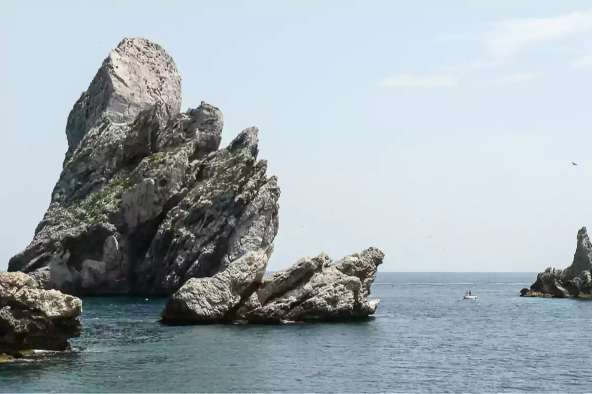 Formacions rocoses sobresortint del mar amb una petita barca al fons en un dia assolellat Formacions rocoses sobresortint del mar amb una petita barca al fons en un dia assolellat