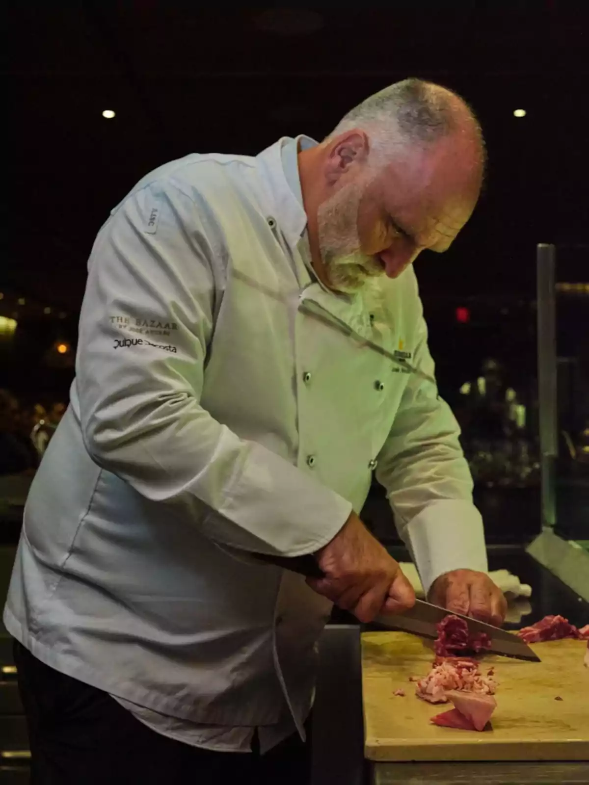Chef de cabello canoso y barba corta cortando carne sobre una tabla en una cocina profesional Chef de cabello canoso y barba corta cortando carne sobre una tabla en una cocina profesional