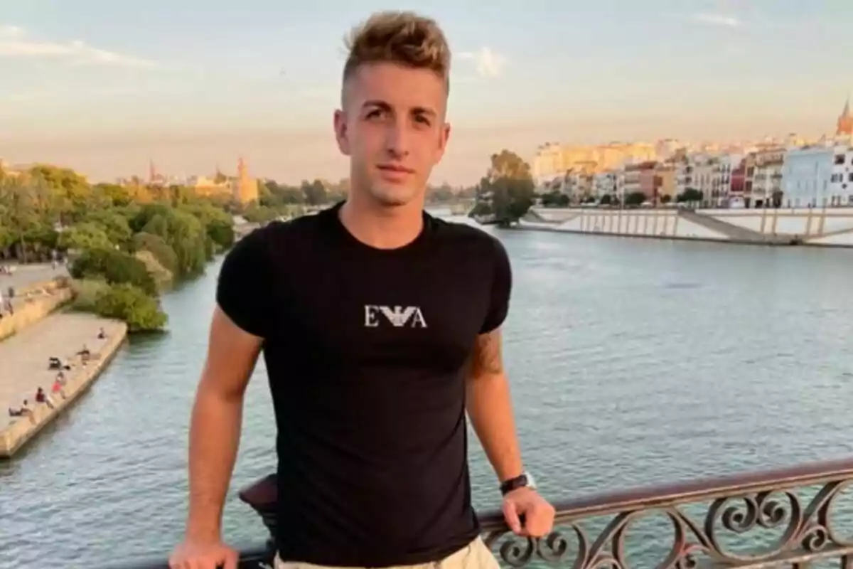 Joven de pie sobre un puente con un río y edificios al fondo en una ciudad al atardecer Joven de pie sobre un puente con un río y edificios al fondo en una ciudad al atardecer