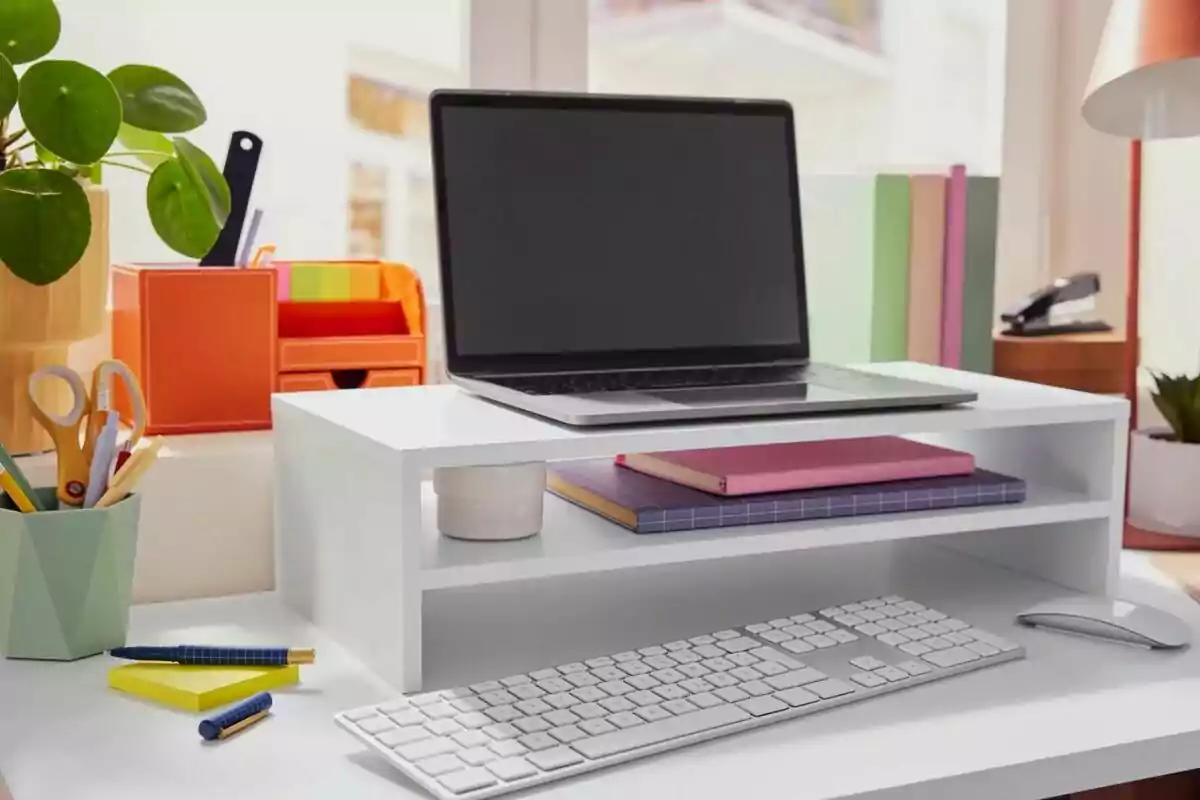 Escriptori endreçat amb un portàtil sobre un suport blanc, teclat, ratolí, quaderns, plantes i material d’oficina. Escriptori endreçat amb un portàtil sobre un suport blanc, teclat, ratolí, quaderns, plantes i material d’oficina.