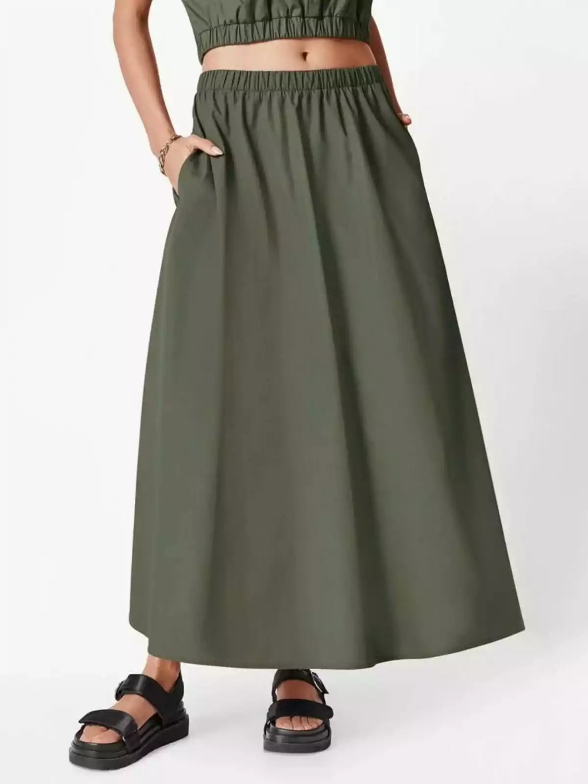 Mujer usando falda larga verde olivo con cintura elástica y sandalias negras Mujer usando falda larga verde olivo con cintura elástica y sandalias negras