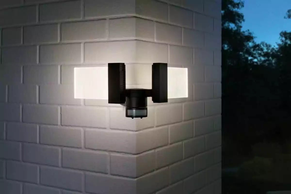 Lámpara de pared moderna encendida en la esquina de una pared de ladrillo blanco al anochecer Lámpara de pared moderna encendida en la esquina de una pared de ladrillo blanco al anochecer