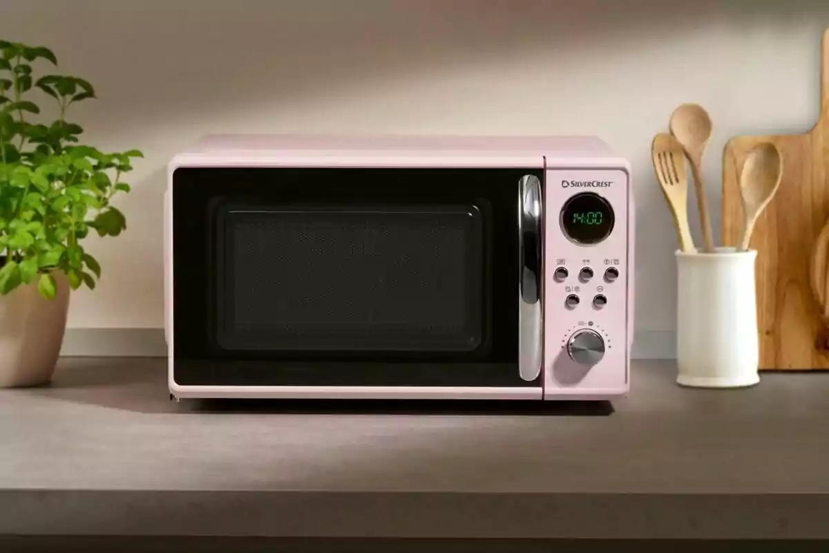 Microondas rosa sobre una encimera de cocina junto a una planta y utensilios de madera Microondas rosa sobre una encimera de cocina junto a una planta y utensilios de madera
