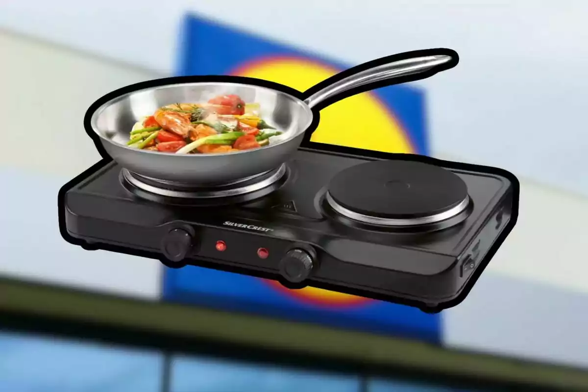 Cuina elèctrica de dos fogons amb paella d’acer inoxidable i verdures saltejades al davant d’un fons desenfocat amb colors blau i groc Cuina elèctrica de dos fogons amb paella d’acer inoxidable i verdures saltejades al davant d’un fons desenfocat amb colors blau i groc