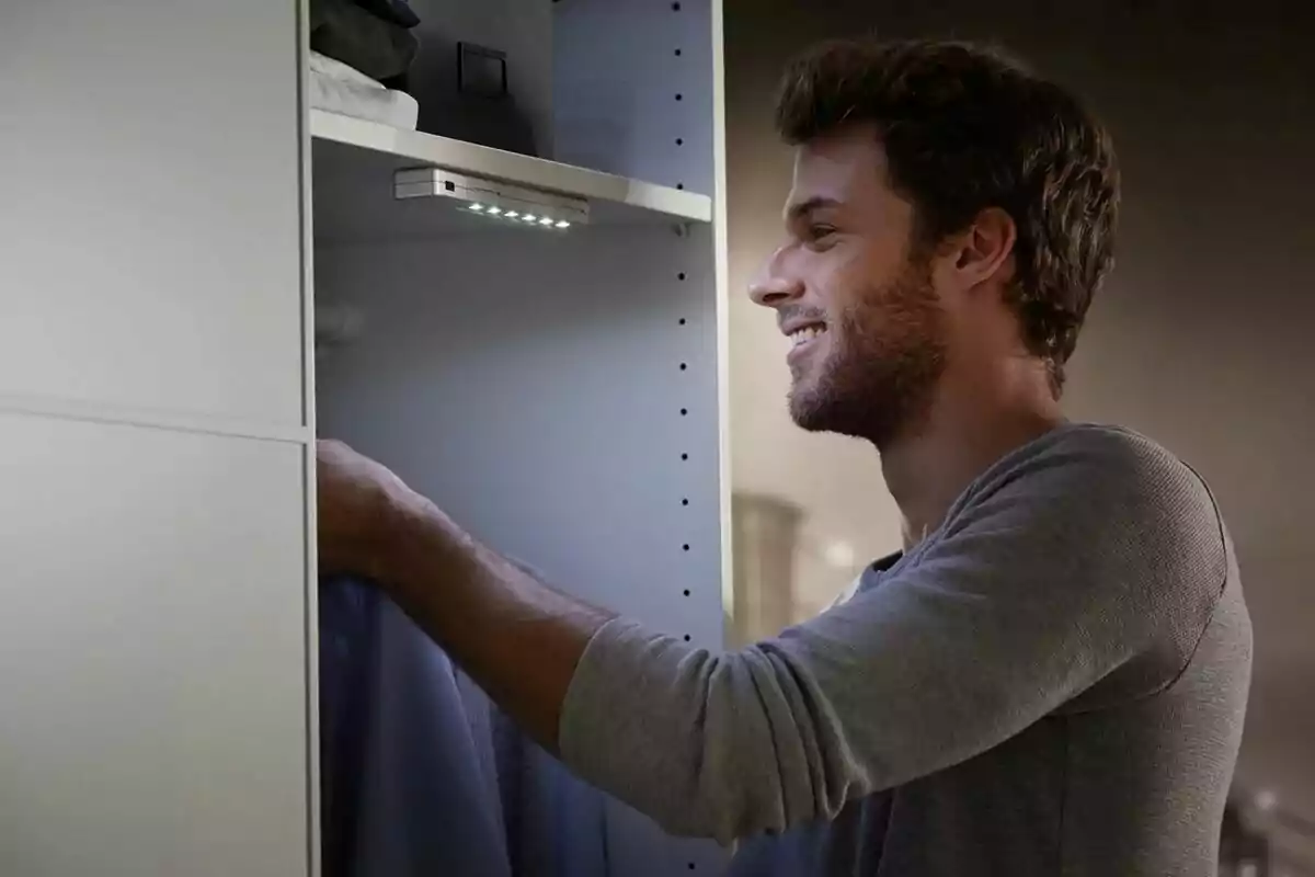Hombre sonriente eligiendo ropa en un armario iluminado por una luz LED Hombre sonriente eligiendo ropa en un armario iluminado por una luz LED