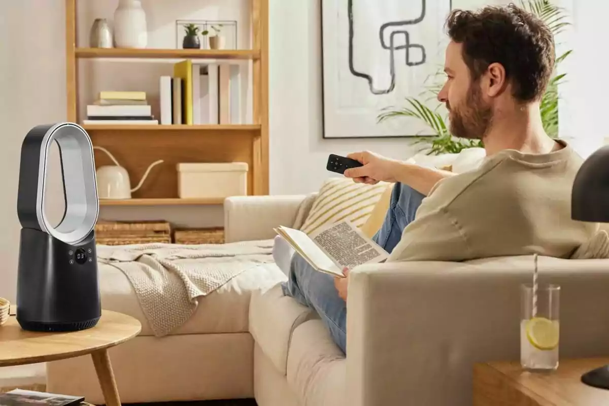 Man sitting on a sofa reading a book and using a remote control to turn on a modern bladeless fan in a cozy living room Man sitting on a sofa reading a book and using a remote control to turn on a modern bladeless fan in a cozy living room