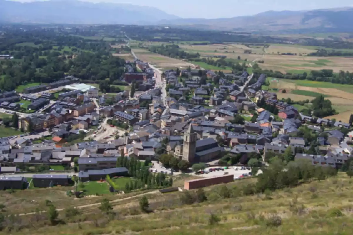 Vista panorámica de un pequeño pueblo rodeado de campos verdes y montañas al fondo Vista panorámica de un pequeño pueblo rodeado de campos verdes y montañas al fondo