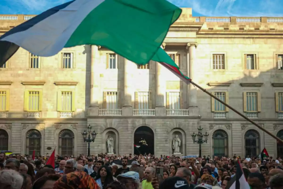 Una multitud de personas se reúne frente a un edificio histórico mientras ondea una gran bandera palestina sobre la multitud Una multitud de personas se reúne frente a un edificio histórico mientras ondea una gran bandera palestina sobre la multitud