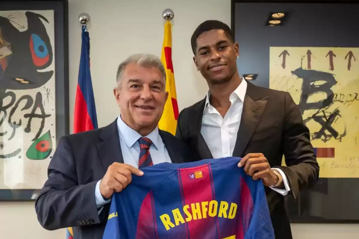 Dos homes posen somrients mentre sostenen una samarreta del FC Barcelona amb el nom Rashford en un despatx decorat amb banderes i quadres del club. Dos homes posen somrients mentre sostenen una samarreta del FC Barcelona amb el nom Rashford en un despatx decorat amb banderes i quadres del club.