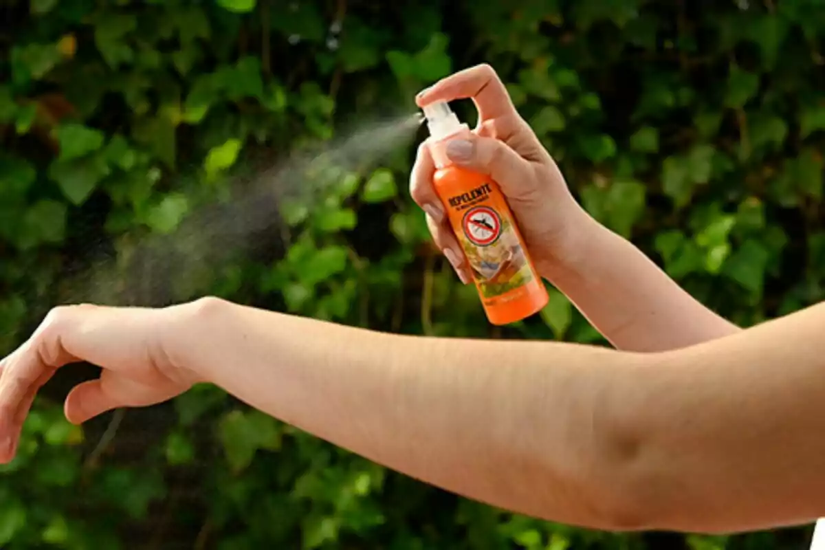 Persona aplicando repelente en spray sobre su brazo con un fondo de plantas verdes Persona aplicando repelente en spray sobre su brazo con un fondo de plantas verdes