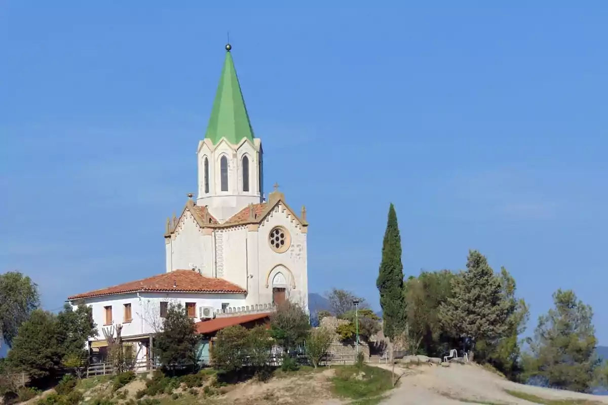 Iglesia blanca con techo de tejas y torre con tejado verde rodeada de árboles bajo un cielo despejado Iglesia blanca con techo de tejas y torre con tejado verde rodeada de árboles bajo un cielo despejado
