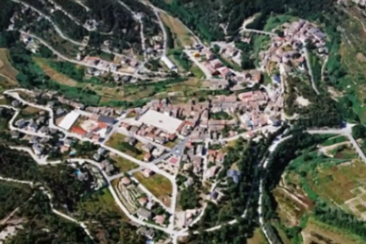 Vista aèria d’un petit poble envoltat de vegetació i muntanyes Vista aèria d’un petit poble envoltat de vegetació i muntanyes