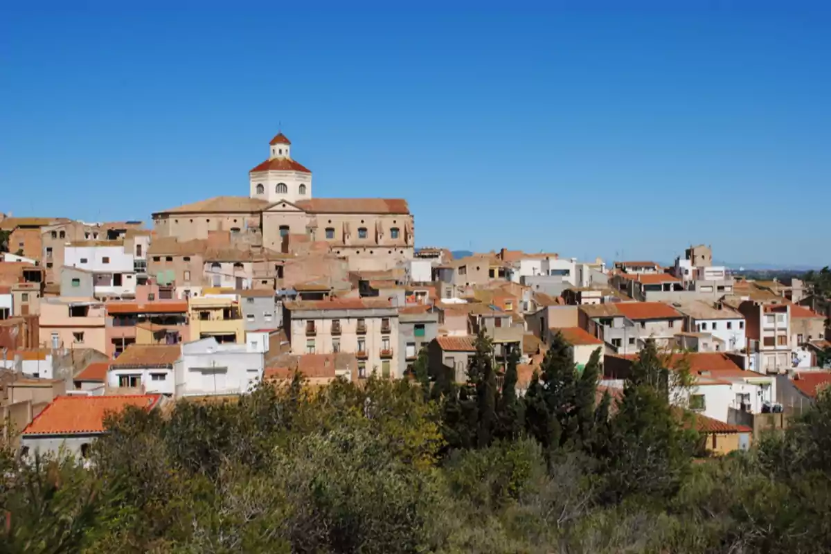 Vista panorámica de un pueblo con casas de tejados rojizos y una iglesia grande en la parte superior bajo un cielo despejado Vista panorámica de un pueblo con casas de tejados rojizos y una iglesia grande en la parte superior bajo un cielo despejado