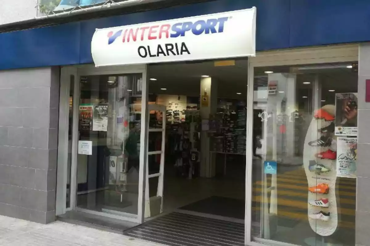 Fachada de una tienda de deportes Intersport Olaria con puertas de cristal y un expositor de zapatillas deportivas en la entrada Fachada de una tienda de deportes Intersport Olaria con puertas de cristal y un expositor de zapatillas deportivas en la entrada