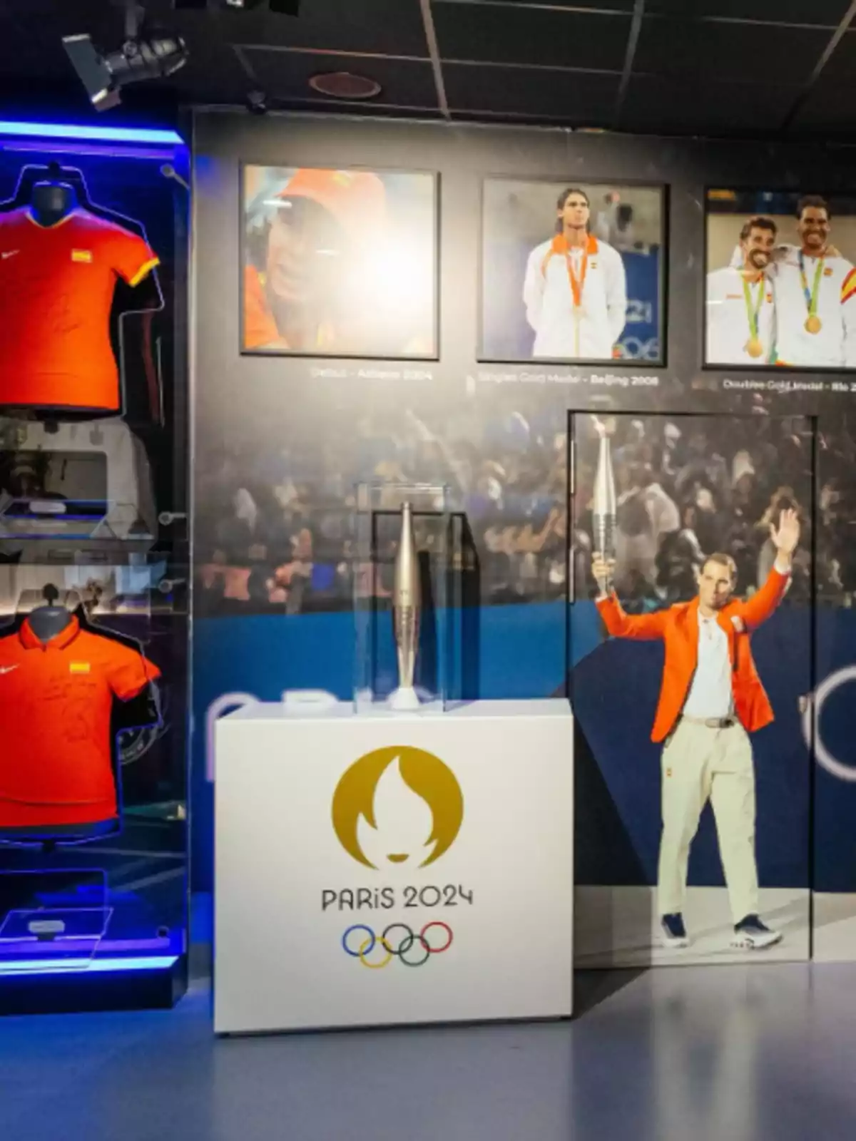 Exhibición de camisetas deportivas firmadas, fotografías de atletas olímpicos y la antorcha de los Juegos Olímpicos de París 2024 en una vitrina Exhibición de camisetas deportivas firmadas, fotografías de atletas olímpicos y la antorcha de los Juegos Olímpicos de París 2024 en una vitrina